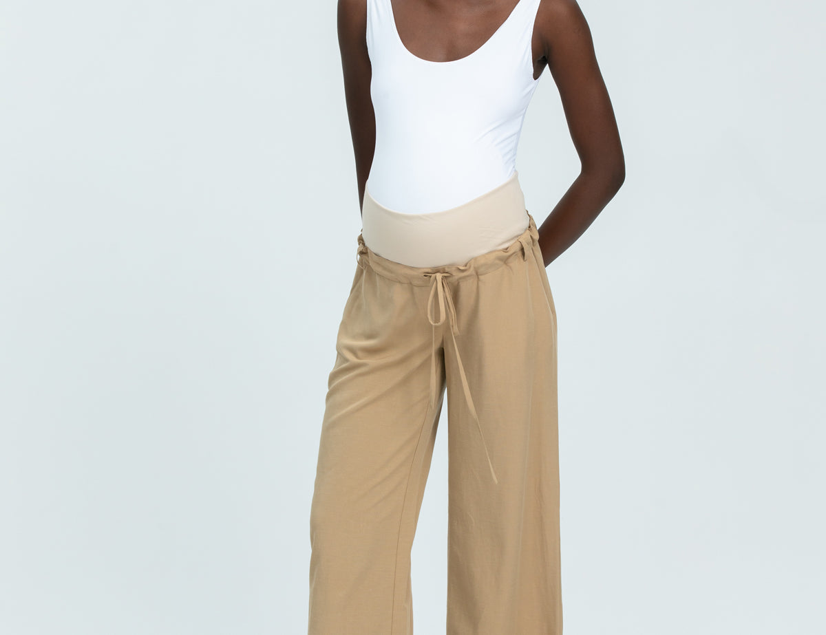 Woman wearing a white tank top and beige wide-leg pants on a white background