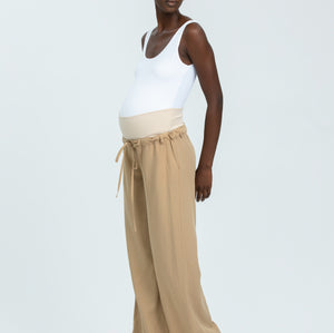 Woman wearing a white tank top and beige wide-leg pants on a white background