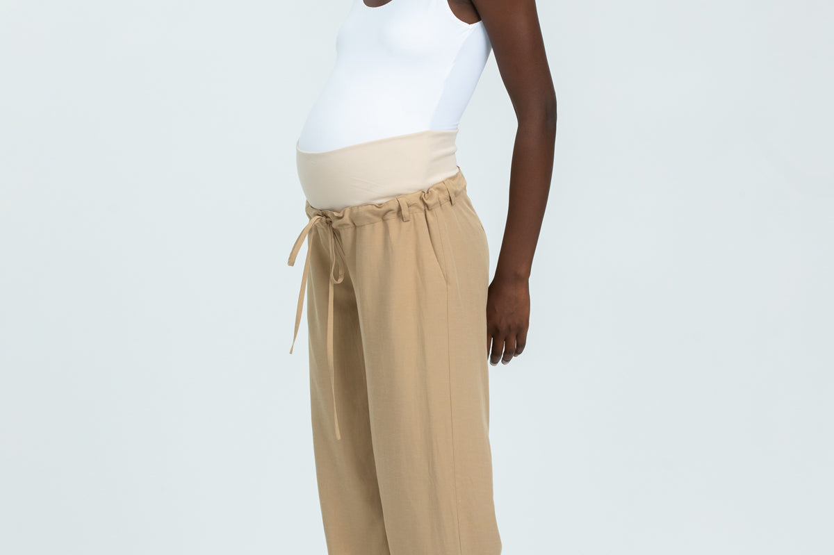 Woman wearing a white tank top and beige wide-leg pants on a white background