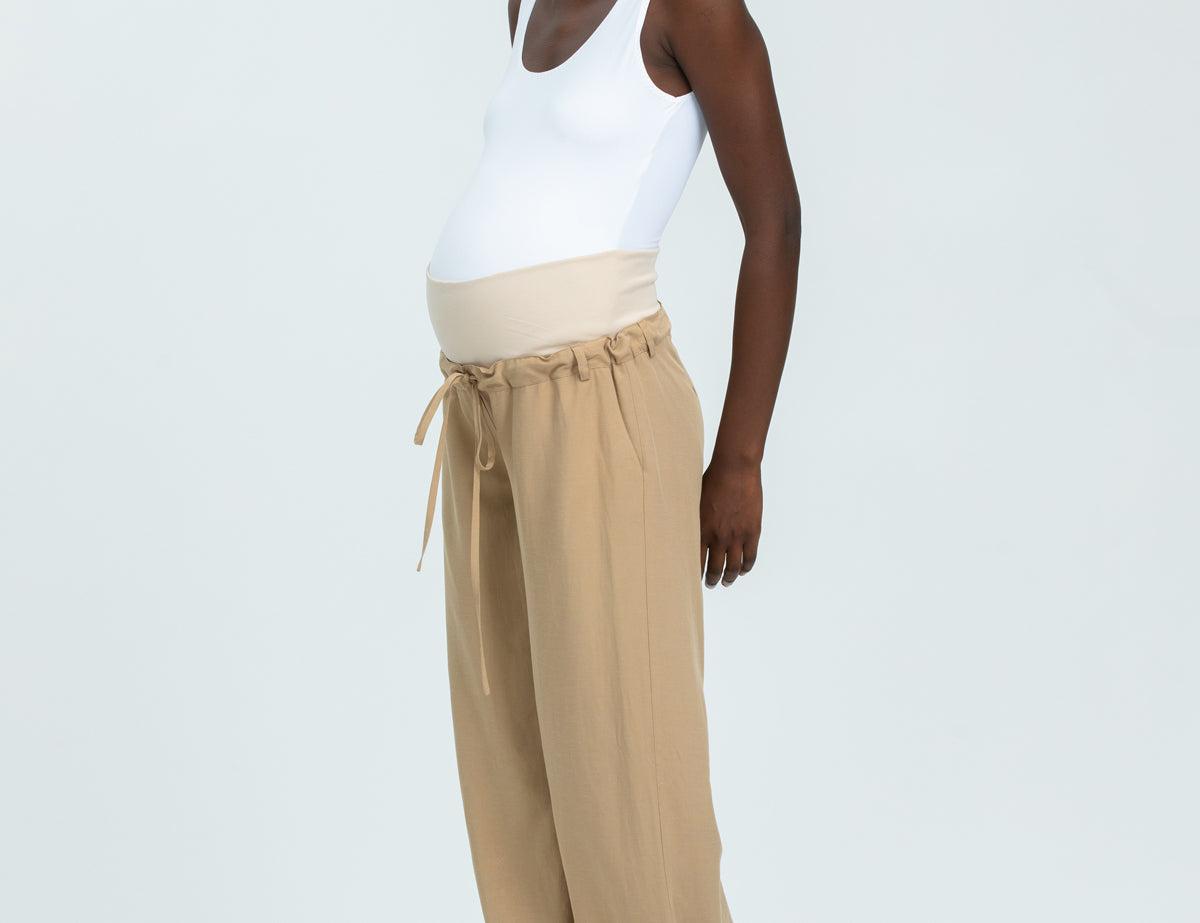 Woman wearing a white tank top and beige wide-leg pants on a white background