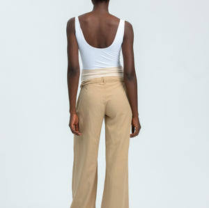 Person wearing a white tank top and beige pants on a light gray background