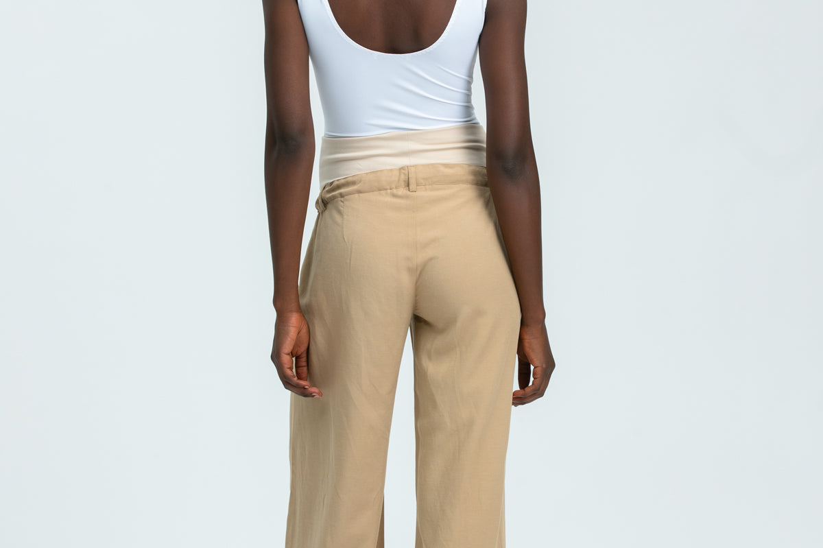 Person wearing a white tank top and beige pants on a light gray background