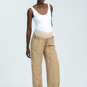 Woman wearing a white tank top and beige pants on a light gray background