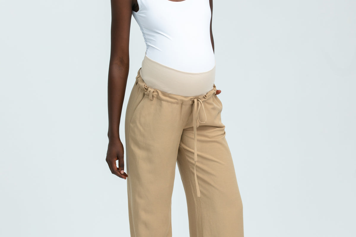 Woman wearing a white tank top and beige pants on a light gray background