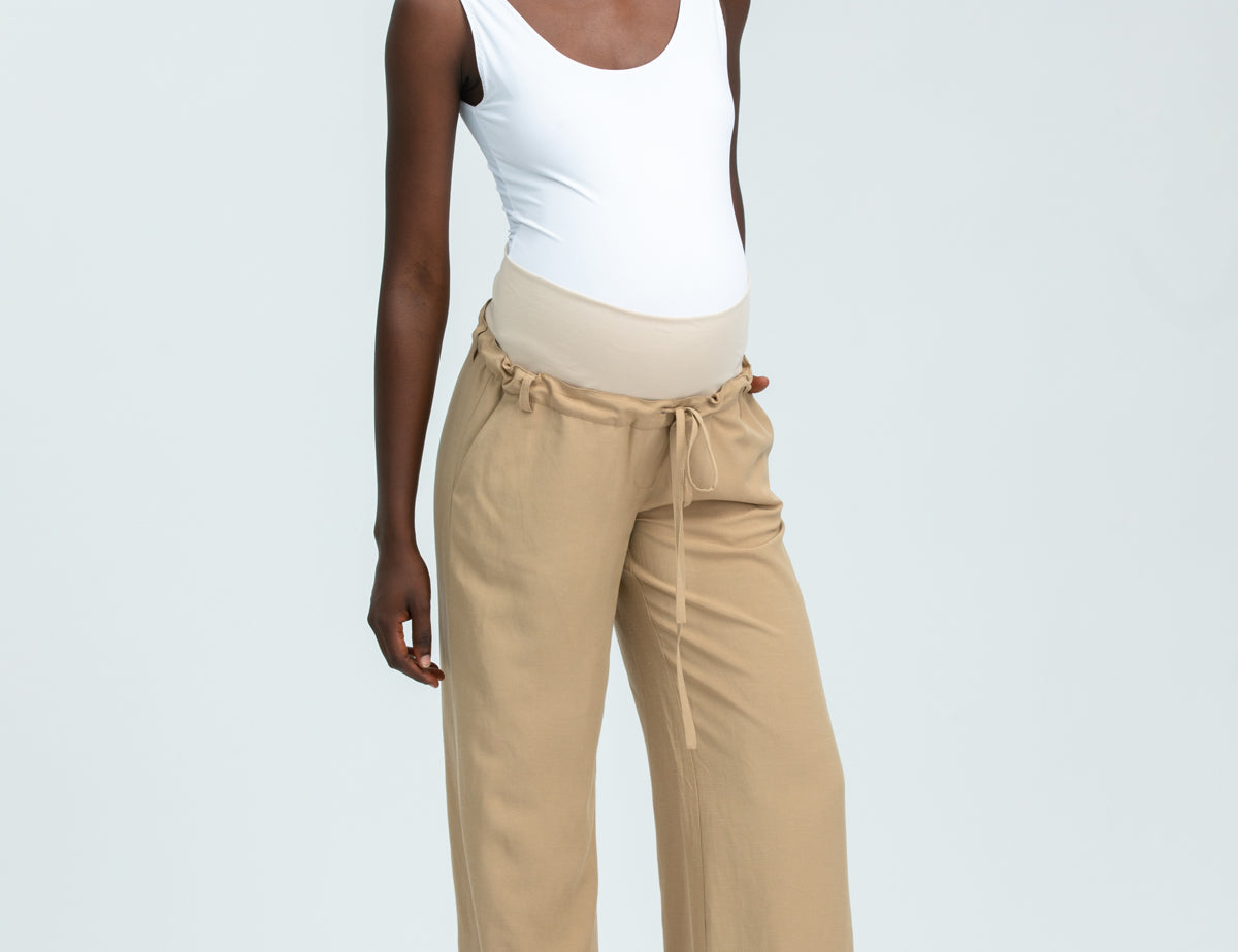 Woman wearing a white tank top and beige pants on a light gray background
