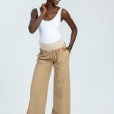 Woman wearing a white tank top and beige wide-leg pants on a light gray background