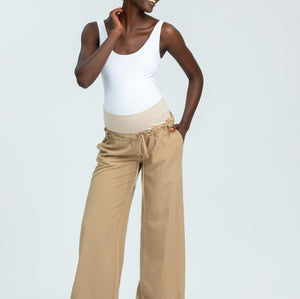 Woman wearing a white tank top and beige wide-leg pants on a light gray background