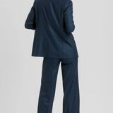 A woman wearing a navy blue two-piece suit, shown from the back, standing against a light gray studio background.