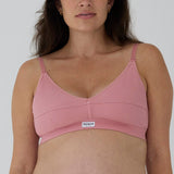 A close-up of a woman wearing a pink ribbed wireless nursing bra with adjustable straps and a small white brand label reading 'RENUE' on the front.