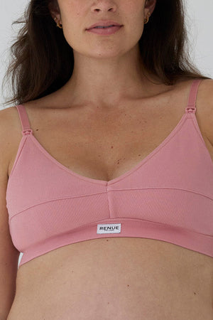 A close-up of a woman wearing a pink ribbed wireless nursing bra with adjustable straps and a small white brand label reading 'RENUE' on the front.