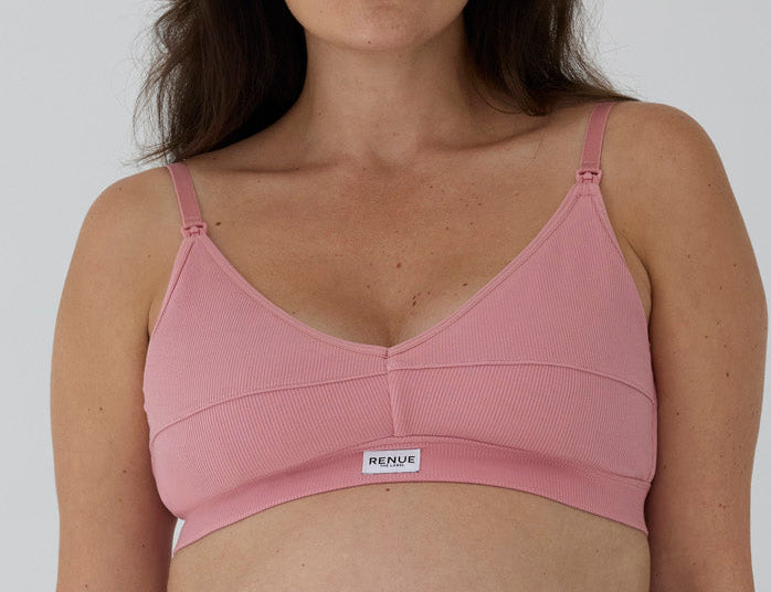 A close-up of a woman wearing a pink ribbed wireless nursing bra with adjustable straps and a small white brand label reading 'RENUE' on the front.