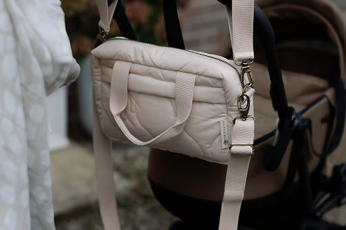 Neutral quilted baby changing bag by Ralphie Bear with waterproof lining, zip compartments, and adjustable strap.