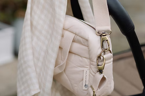 Neutral quilted baby changing bag by Ralphie Bear with waterproof lining, zip compartments, and adjustable strap.