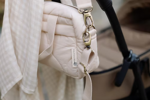 Neutral quilted baby changing bag by Ralphie Bear with waterproof lining, zip compartments, and adjustable strap.