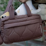 Brown quilted handbag with a cartoon character peeking out, held by a person.