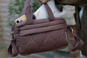 Brown quilted handbag with a cartoon character peeking out, held by a person.