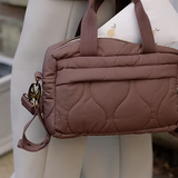 Brown quilted handbag held by a person with a blurred background