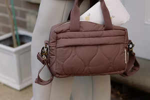 Brown quilted handbag held by a person with a blurred background