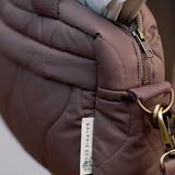 Close-up of a brown quilted bag with a gold zipper and strap, featuring a Ralphie's Bear tag.