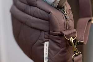 Close-up of a brown quilted bag with a gold zipper and strap, featuring a Ralphie's Bear tag.