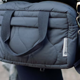 Gray quilted bag with a strap over shoulder on a blurred background