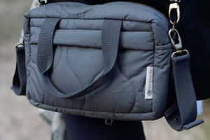 Gray quilted bag with a strap over shoulder on a blurred background