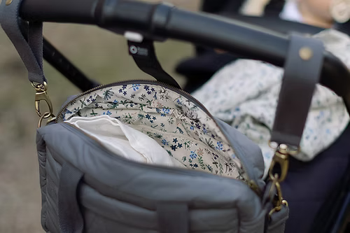 Gray diaper bag with floral lining attached to a stroller