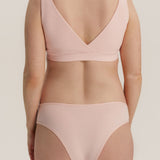 A model shown from the back wearing a light pink two-piece bikini set, featuring a wrap-style bra top and matching high-cut briefs, against a solid light beige background.