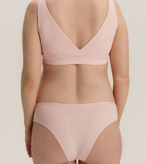 A model shown from the back wearing a light pink two-piece bikini set, featuring a wrap-style bra top and matching high-cut briefs, against a solid light beige background.