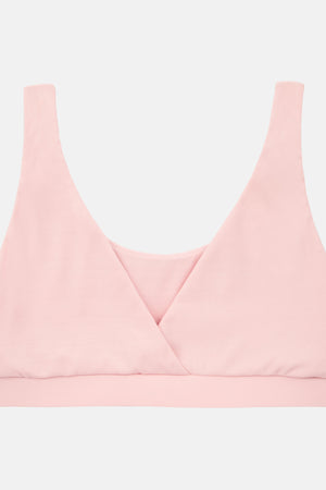A light pink wireless bralette with a wrap-style crossover neckline and wide shoulder straps, shown flat against a light gray background.