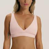 A woman wearing a light pink wrap-style sports bra against a plain light gray studio background.