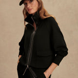 Woman wearing Varley Roxbury zip-through sweatshirt in black DoubleSoft® fabric with high neck and front pockets.