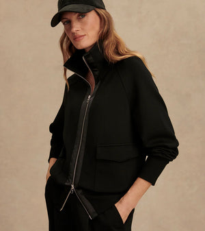 Woman wearing Varley Roxbury zip-through sweatshirt in black DoubleSoft® fabric with high neck and front pockets.