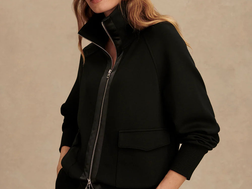 Woman wearing Varley Roxbury zip-through sweatshirt in black DoubleSoft® fabric with high neck and front pockets.