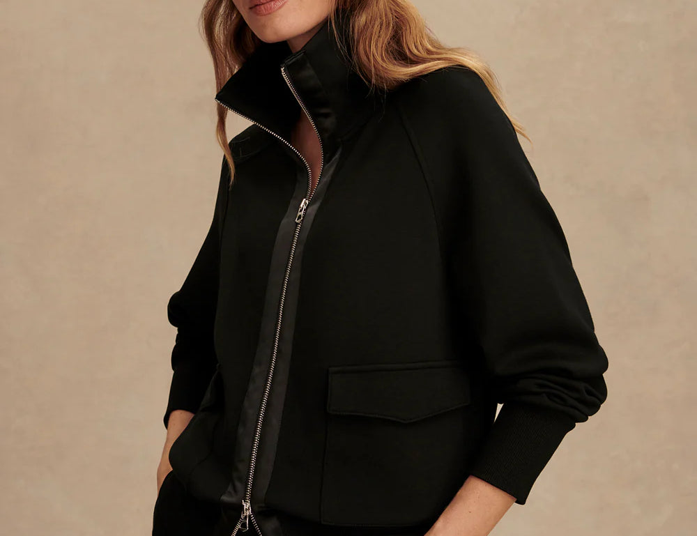 Woman wearing Varley Roxbury zip-through sweatshirt in black DoubleSoft® fabric with high neck and front pockets.