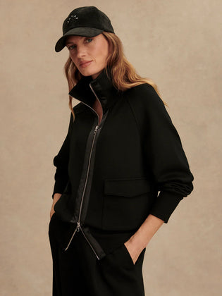 Woman wearing Varley Roxbury zip-through sweatshirt in black DoubleSoft® fabric with high neck and front pockets.