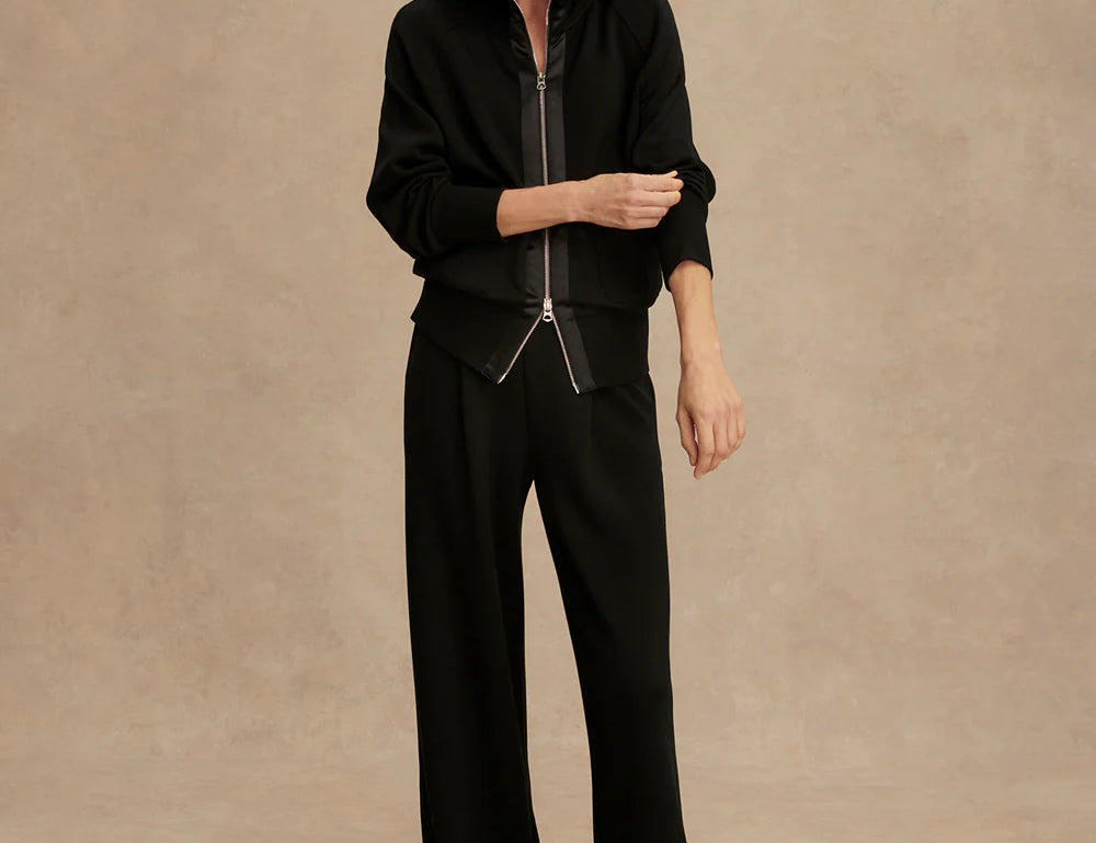 Woman wearing Varley Roxbury zip-through sweatshirt in black DoubleSoft® fabric with high neck and front pockets.