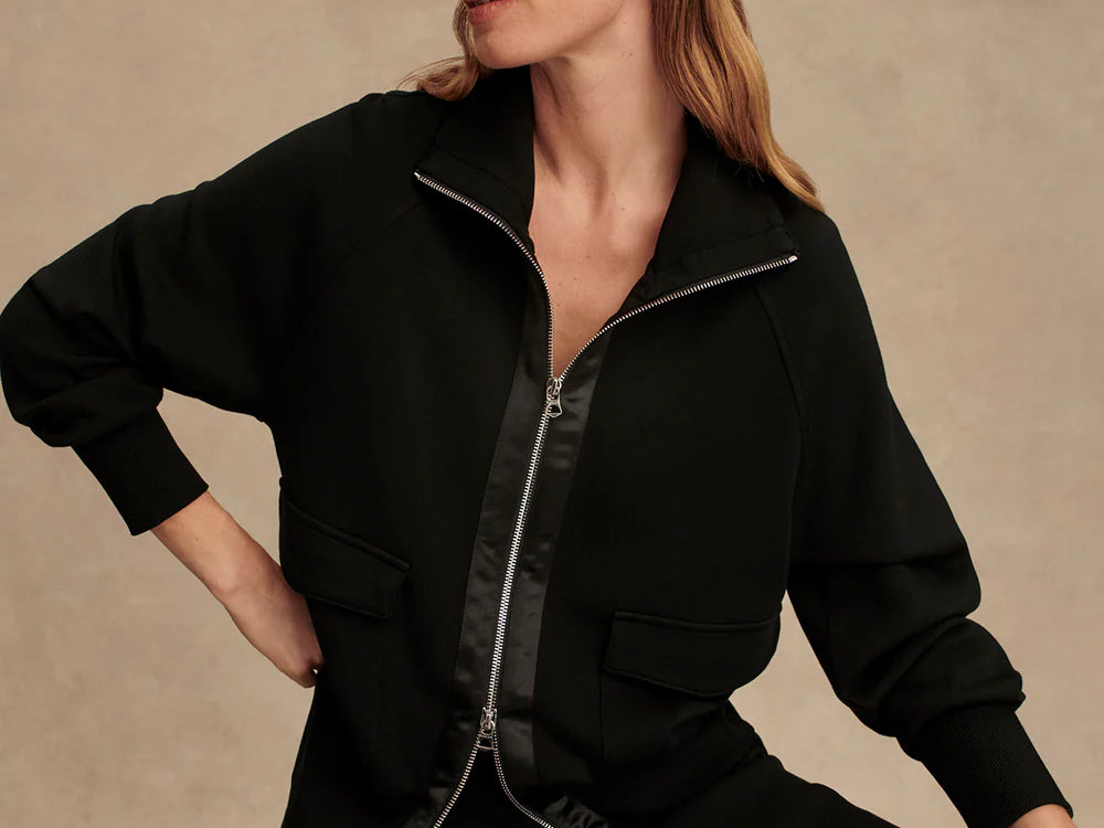 Woman wearing Varley Roxbury zip-through sweatshirt in black DoubleSoft® fabric with high neck and front pockets.