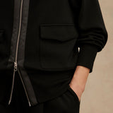 Woman wearing Varley Roxbury zip-through sweatshirt in black DoubleSoft® fabric with high neck and front pockets.