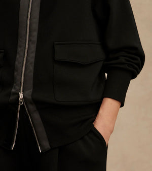 Woman wearing Varley Roxbury zip-through sweatshirt in black DoubleSoft® fabric with high neck and front pockets.