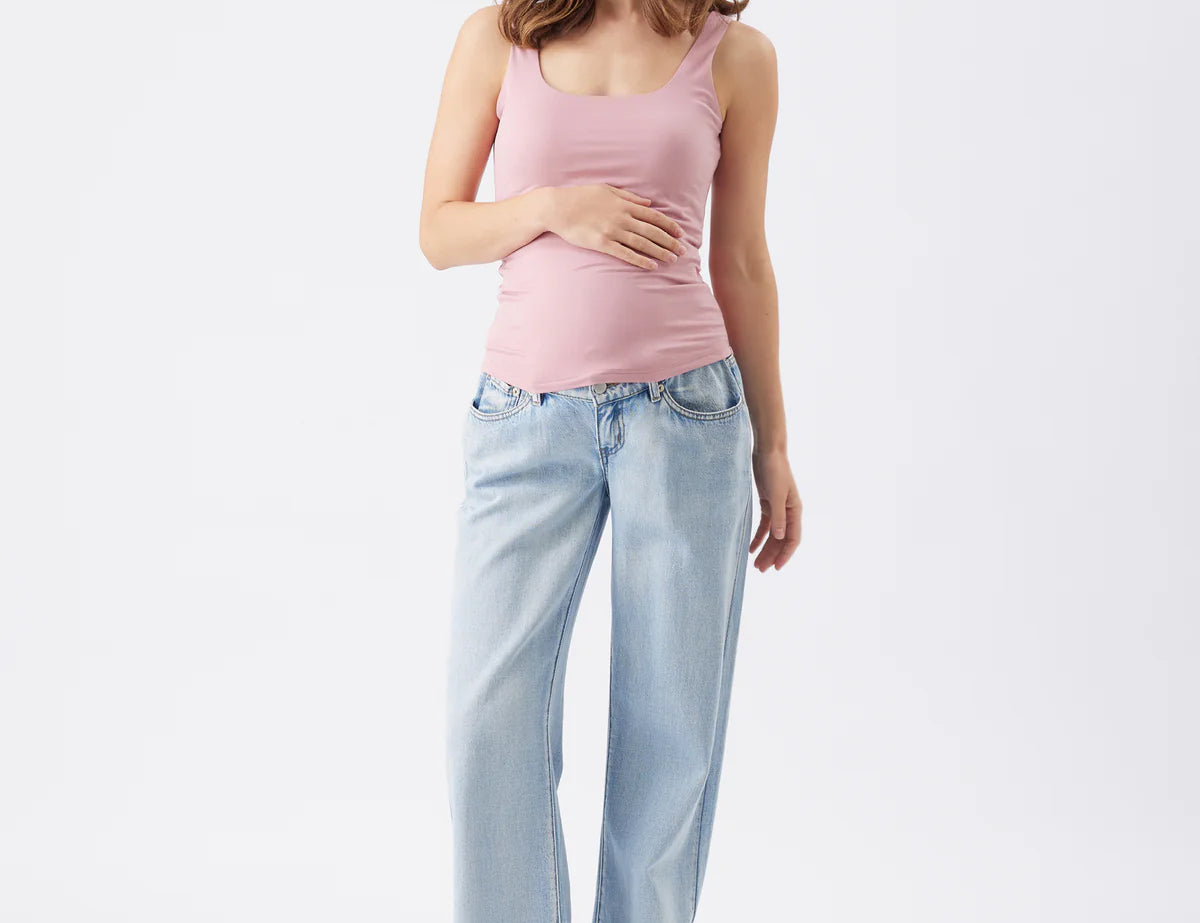 Woman wearing a pink tank top and light blue jeans on a white background