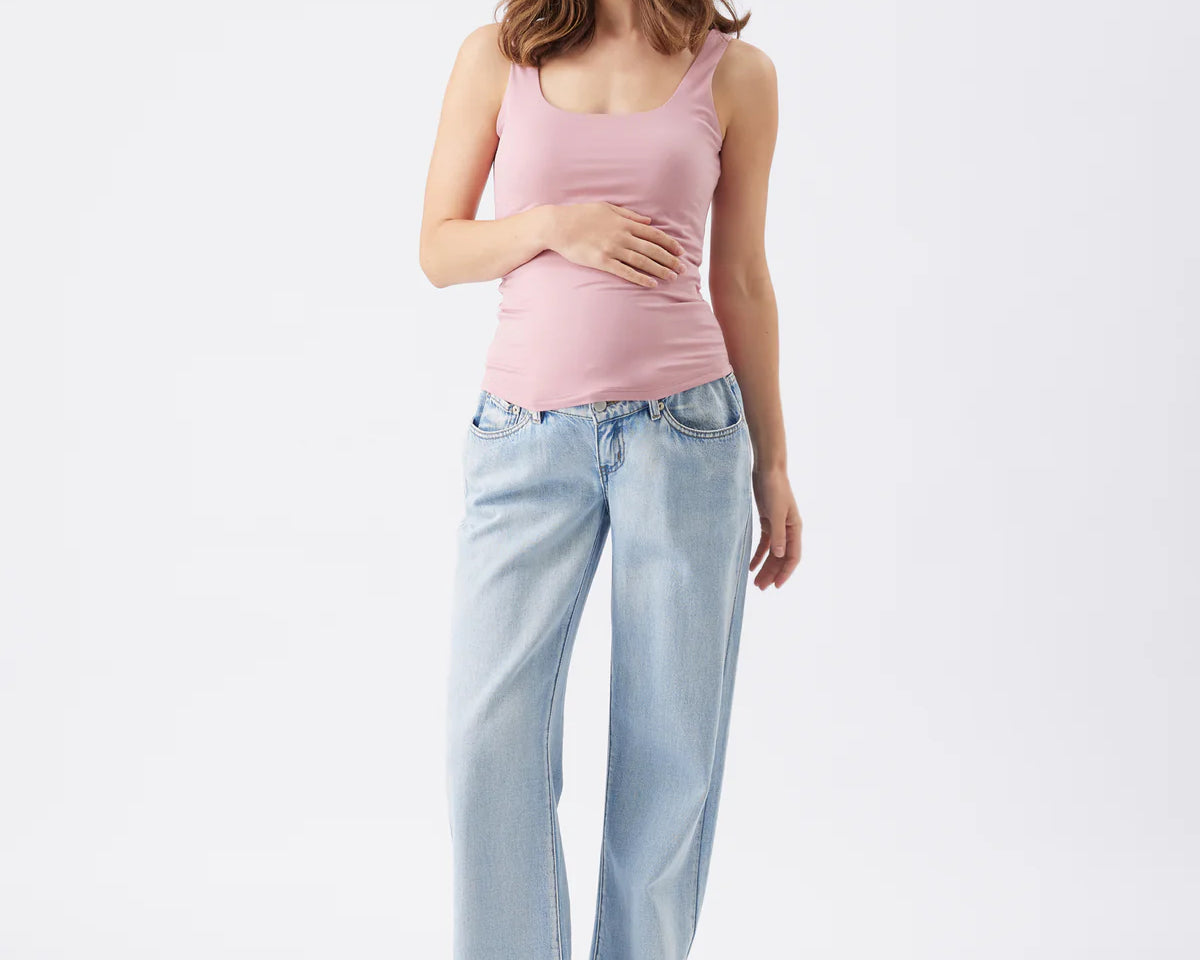 Woman wearing a pink tank top and light blue jeans on a white background