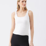 Woman wearing a white tank top and black leggings against a light gray background