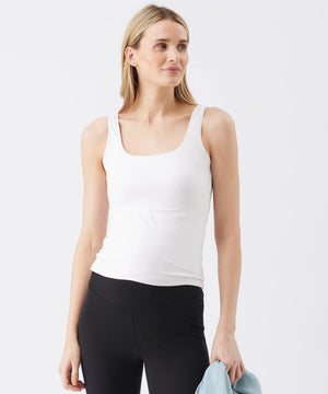 Woman wearing a white tank top and black leggings against a light gray background
