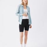 Woman wearing a light blue denim jacket, white top, and black shorts on a white background
