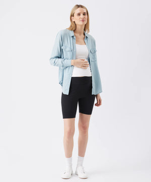 Woman wearing a light blue denim jacket, white top, and black shorts on a white background