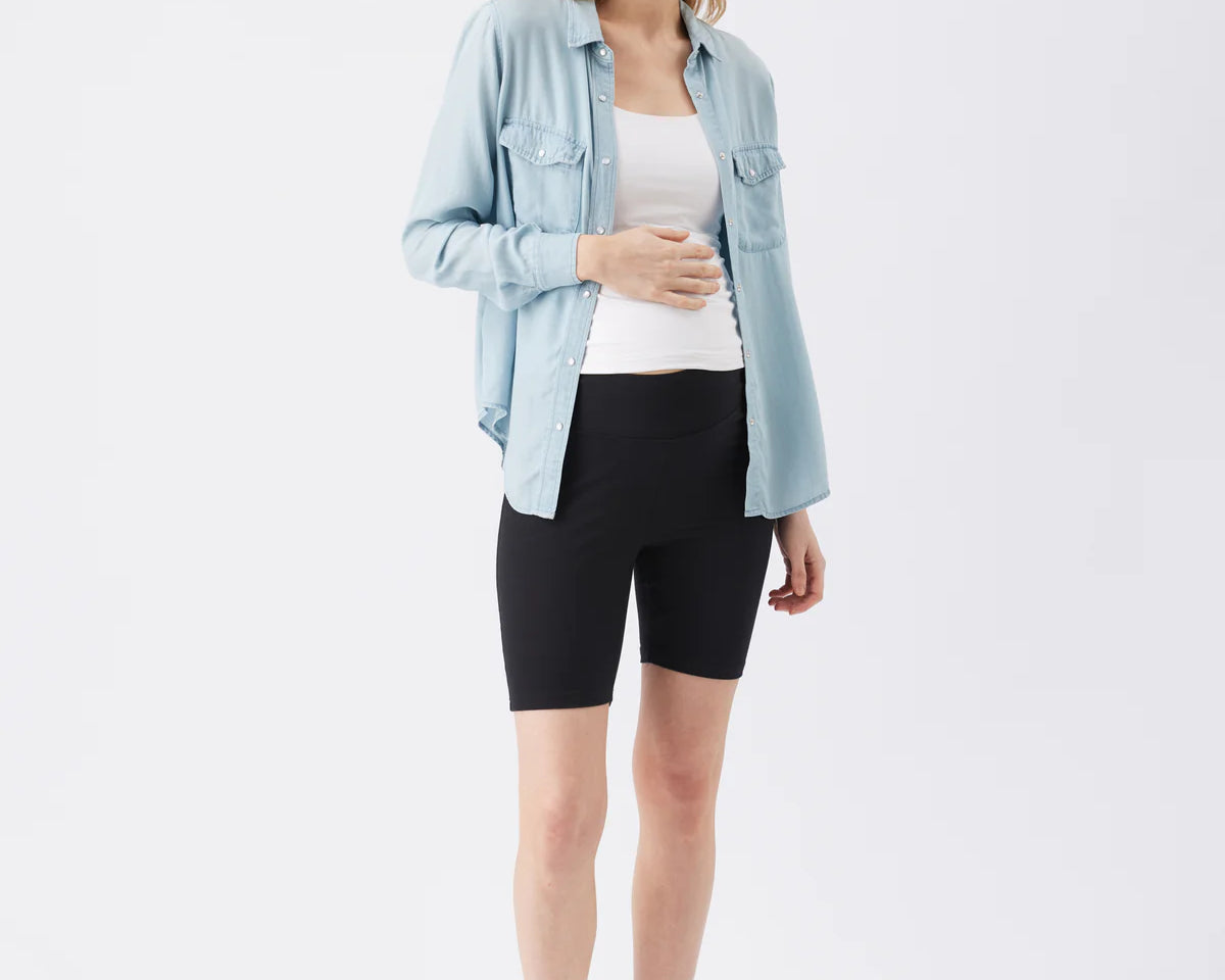 Woman wearing a light blue denim jacket, white top, and black shorts on a white background