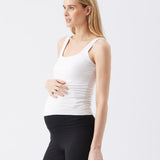 Woman wearing a white tank top and black pants on a light gray background