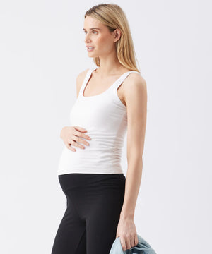 Woman wearing a white tank top and black pants on a light gray background