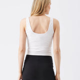 Woman wearing a white tank top and black leggings on a plain background